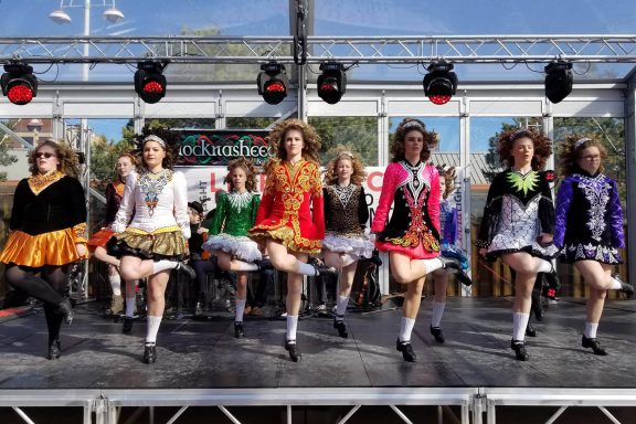 Dances in colorful outfits on an outdoor stage.